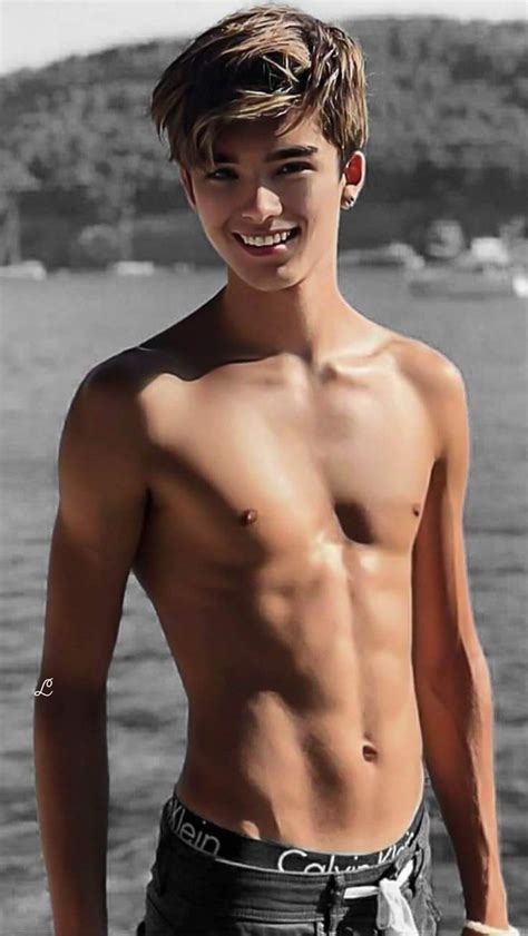 a shirtless young man standing next to the ocean with his hands in his ...